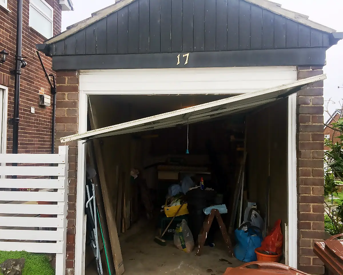 Up-and-over garage door dropped at one side, hanging at an angle across the opening