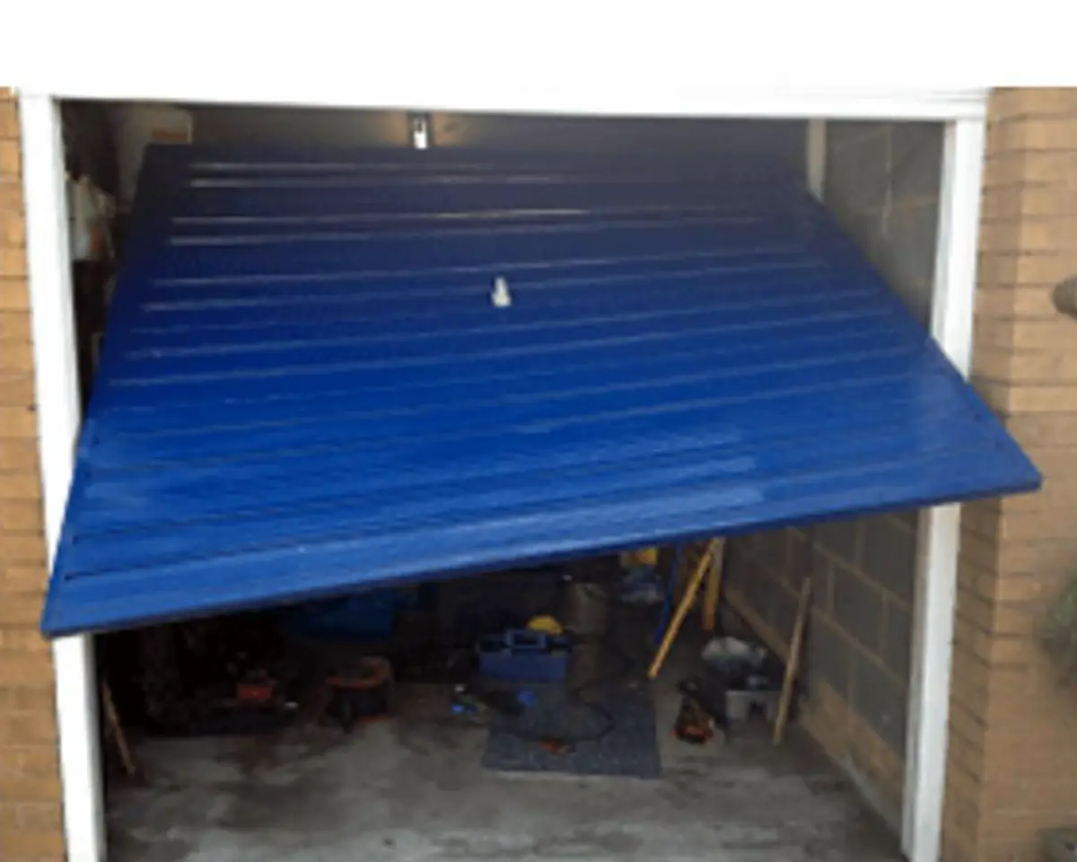 Blue ribbed garage door dropped at one side, hanging crooked and half open